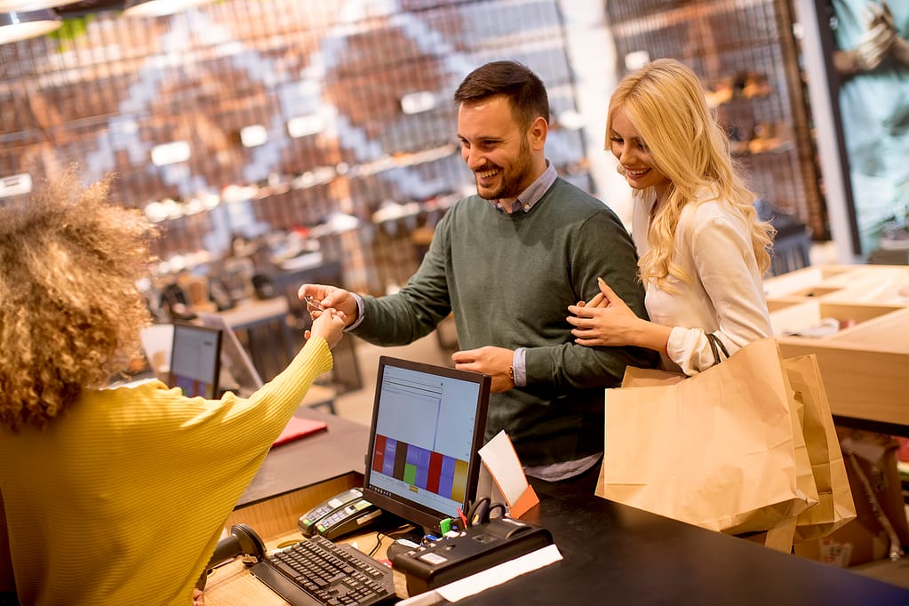 Young couple paying female sales assistant with credit card in c