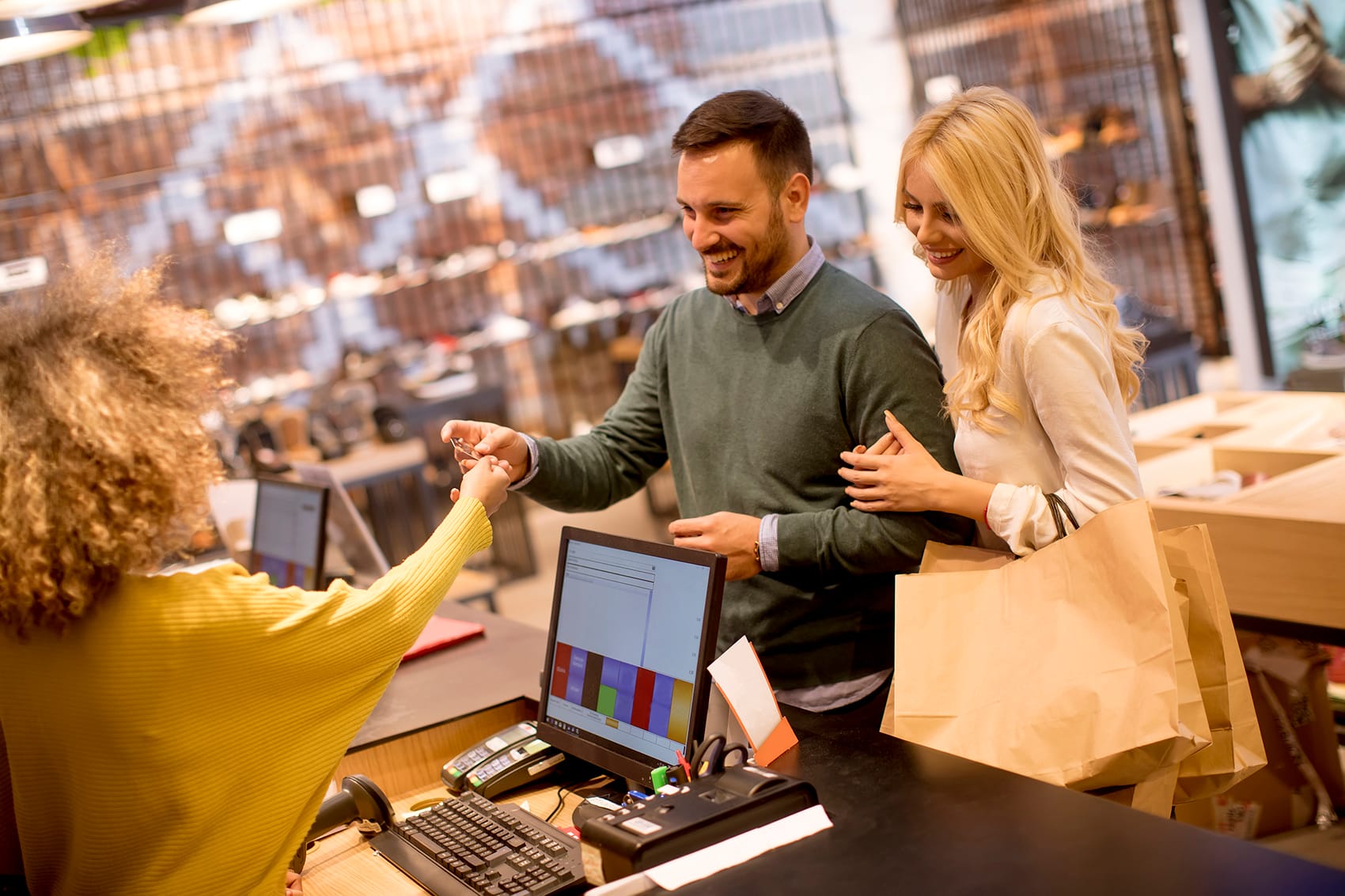 Young couple paying female sales assistant with credit card in c